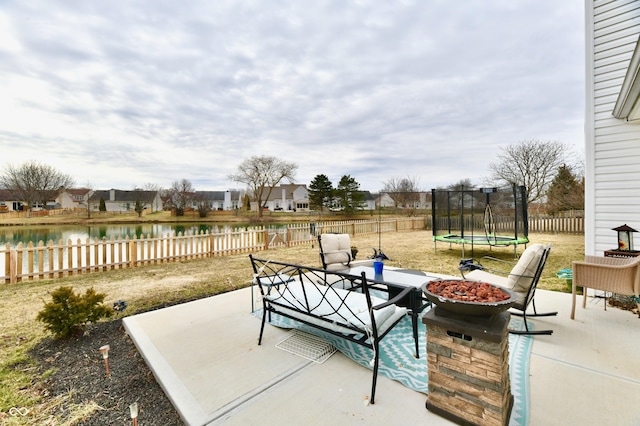 view of patio / terrace featuring a trampoline, an outdoor fire pit, a fenced backyard, and a water view