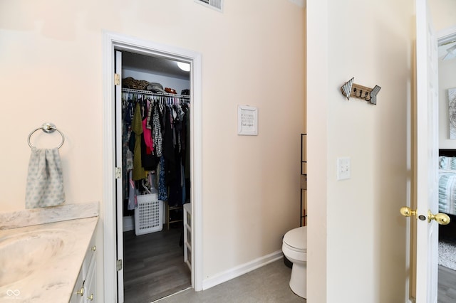 bathroom featuring visible vents, baseboards, toilet, a walk in closet, and vanity