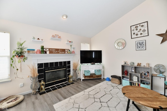 living room featuring baseboards, vaulted ceiling, wood finished floors, and a tile fireplace