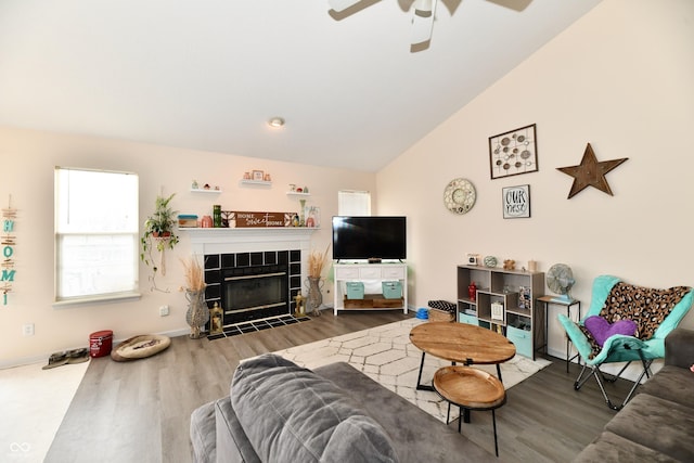 living area featuring baseboards, a tiled fireplace, lofted ceiling, ceiling fan, and wood finished floors