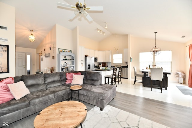 living area with ceiling fan with notable chandelier, high vaulted ceiling, light wood finished floors, and visible vents