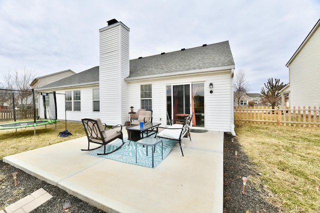 rear view of property featuring a trampoline, a chimney, a shingled roof, a patio area, and fence