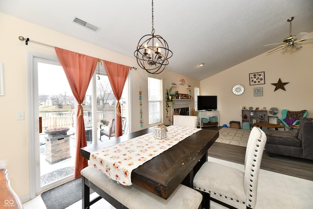 dining room featuring vaulted ceiling, ceiling fan with notable chandelier, a fireplace, and visible vents