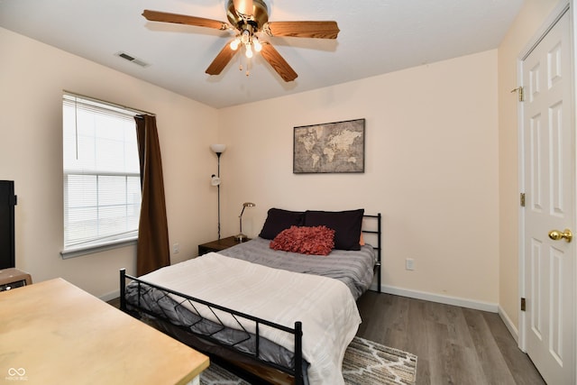 bedroom featuring a ceiling fan, visible vents, baseboards, and wood finished floors