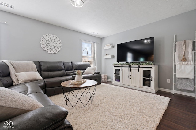 living room featuring a textured ceiling, dark wood-type flooring, visible vents, and baseboards