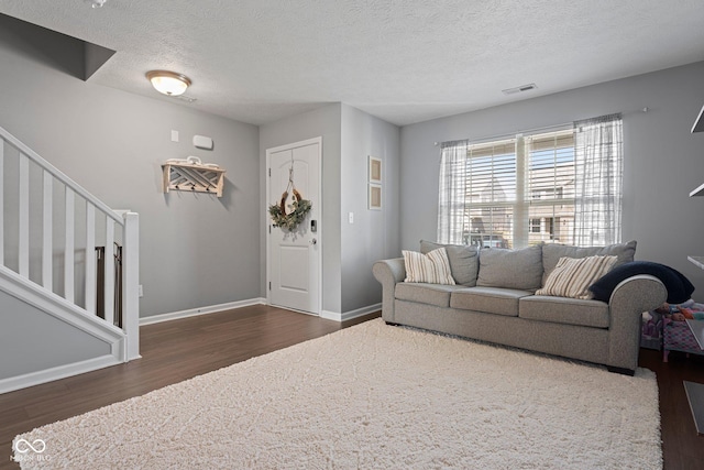 living area featuring baseboards, visible vents, stairway, wood finished floors, and a textured ceiling