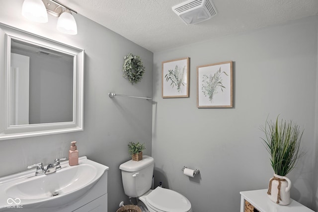 half bath with visible vents, vanity, toilet, and a textured ceiling