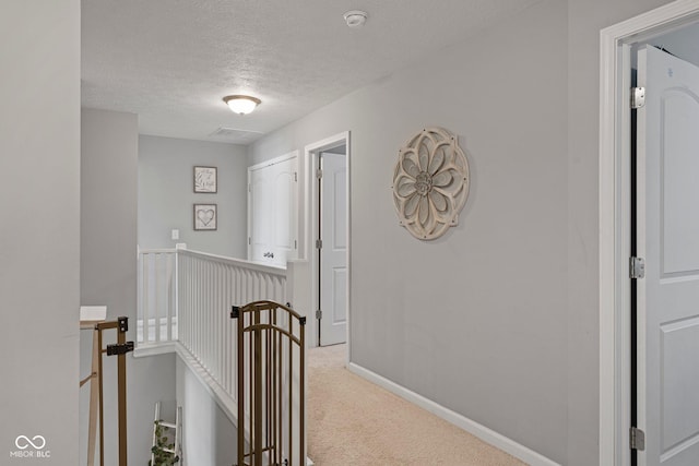 hallway with carpet, baseboards, a textured ceiling, and an upstairs landing