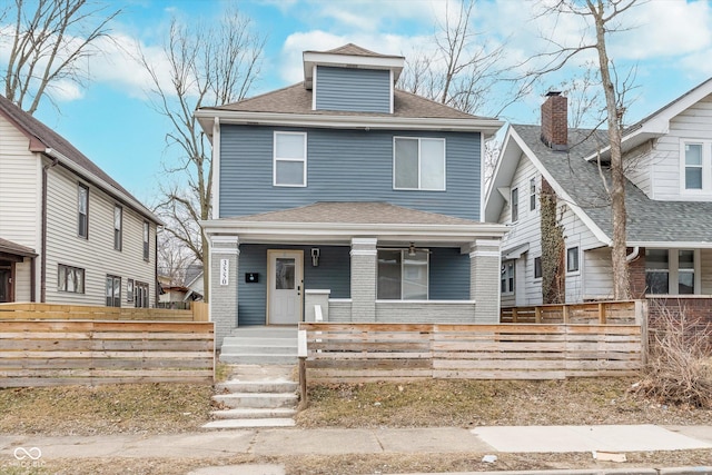 traditional style home featuring roof with shingles, a porch, a fenced front yard, and brick siding