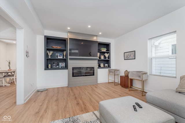 living room featuring built in features, a fireplace, baseboards, and wood finished floors