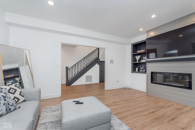 living room with baseboards, built in features, a glass covered fireplace, stairway, and light wood-type flooring