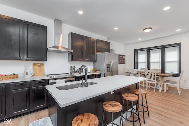 kitchen with a breakfast bar, stainless steel appliances, a sink, wall chimney range hood, and light wood-type flooring