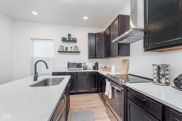 kitchen featuring open shelves, a sink, light countertops, appliances with stainless steel finishes, and wall chimney exhaust hood