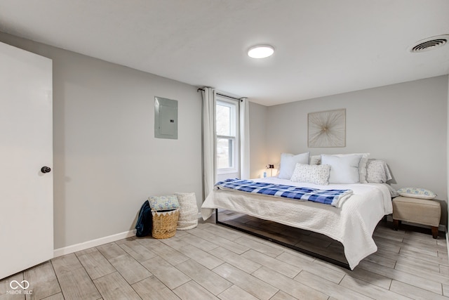 bedroom featuring wood finish floors, electric panel, visible vents, and baseboards