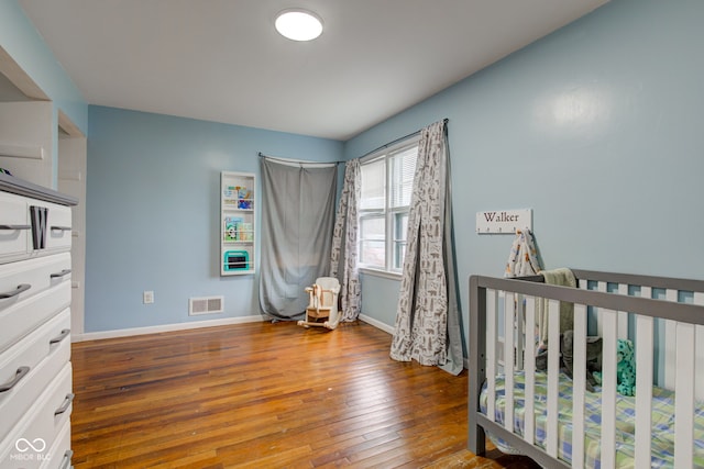 bedroom with a nursery area, baseboards, visible vents, and hardwood / wood-style floors