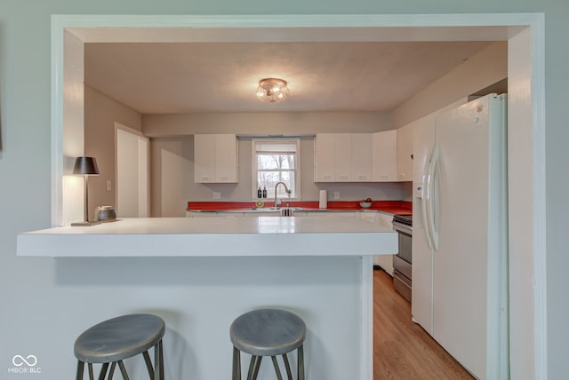 kitchen featuring a breakfast bar, white refrigerator with ice dispenser, stainless steel stove, white cabinetry, and a peninsula