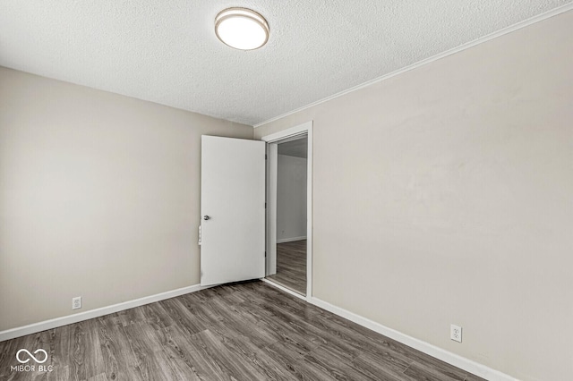 empty room with ornamental molding, a textured ceiling, baseboards, and wood finished floors