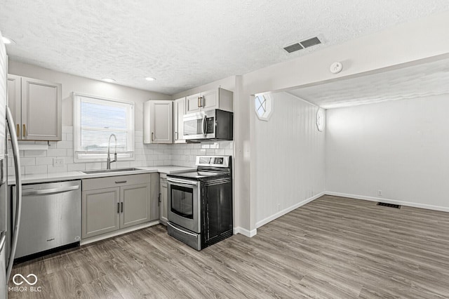 kitchen featuring visible vents, light wood finished floors, a sink, stainless steel appliances, and tasteful backsplash