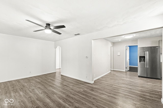 unfurnished room featuring a ceiling fan, wood finished floors, arched walkways, and baseboards