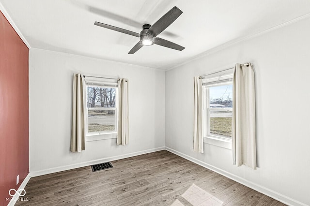 empty room featuring visible vents, a healthy amount of sunlight, crown molding, and wood finished floors