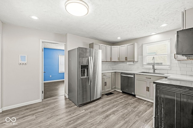 kitchen featuring baseboards, a sink, stainless steel appliances, light wood-style floors, and tasteful backsplash