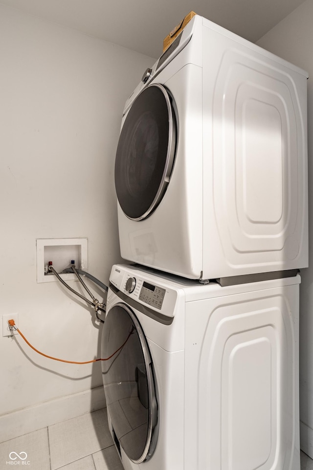 washroom with stacked washer and dryer, tile patterned flooring, laundry area, and baseboards