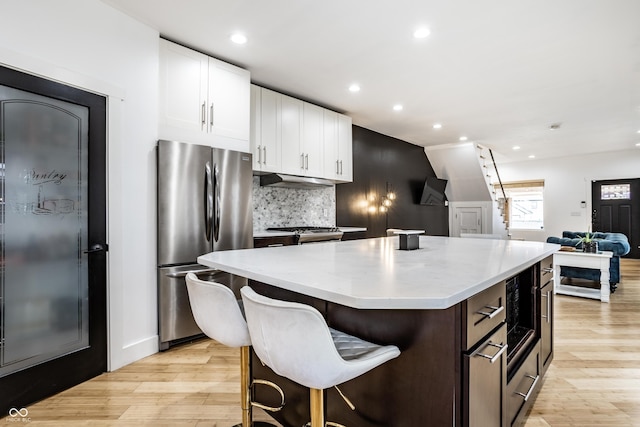 kitchen featuring light wood-style floors, tasteful backsplash, white cabinets, and freestanding refrigerator