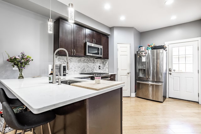 kitchen with appliances with stainless steel finishes, light wood-style floors, a sink, dark brown cabinets, and a peninsula