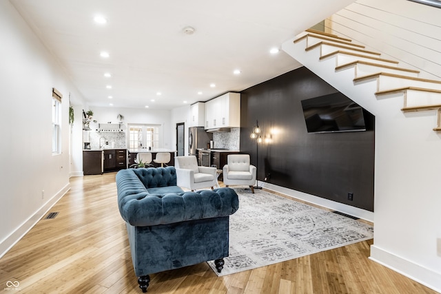 living room featuring recessed lighting, visible vents, light wood-type flooring, baseboards, and stairs