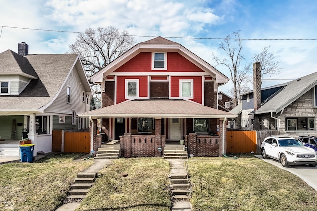 view of front facade featuring a porch, a front yard, brick siding, and fence