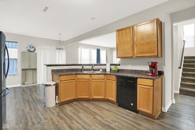 kitchen with a peninsula, a sink, wood finished floors, black appliances, and dark countertops