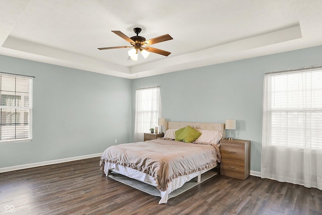 bedroom with dark wood-style flooring, a raised ceiling, and baseboards