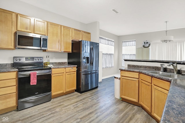 kitchen with visible vents, dark countertops, light wood-style flooring, stainless steel appliances, and a sink