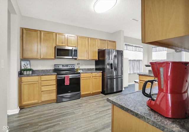 kitchen featuring visible vents, baseboards, dark countertops, appliances with stainless steel finishes, and light wood-style floors