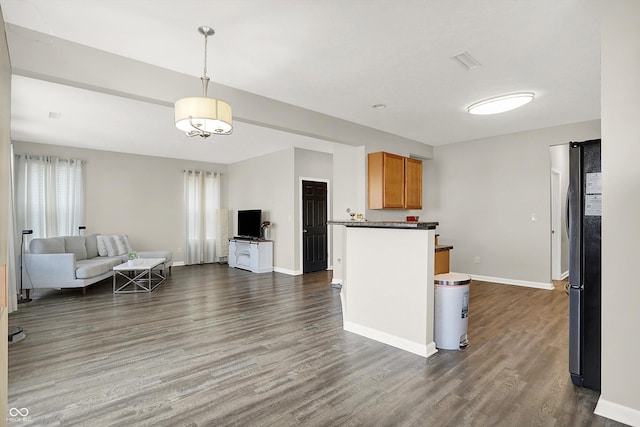 kitchen featuring dark wood-style flooring, baseboards, open floor plan, freestanding refrigerator, and dark countertops