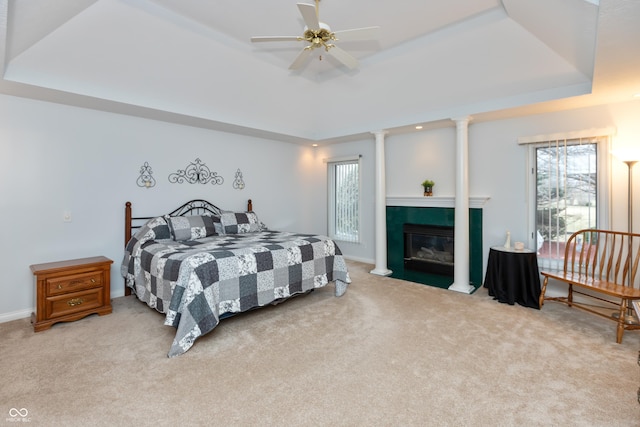 bedroom featuring carpet floors, a fireplace with flush hearth, baseboards, a tray ceiling, and decorative columns