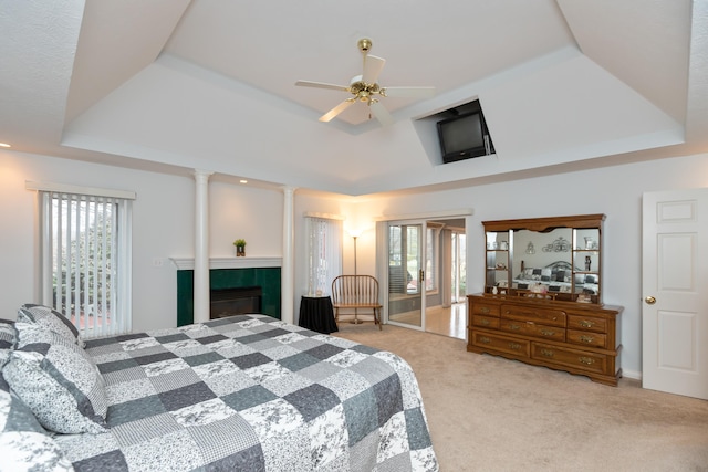 bedroom featuring ceiling fan, a fireplace, carpet, a raised ceiling, and decorative columns