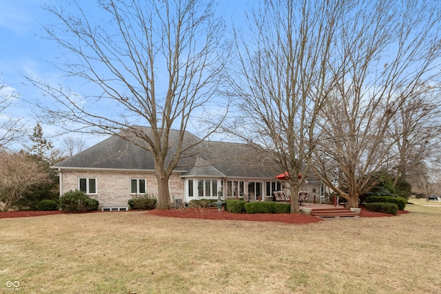 back of property with brick siding, a shingled roof, a deck, and a yard