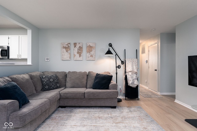 living room featuring light wood-style floors, visible vents, and baseboards