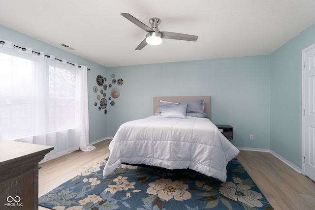 bedroom with ceiling fan, wood finished floors, visible vents, and baseboards