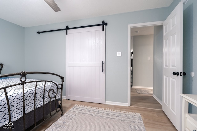 bedroom featuring ceiling fan, a barn door, light wood-type flooring, and baseboards