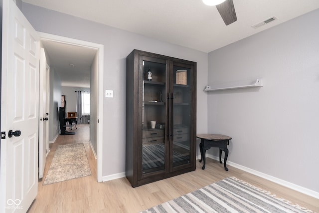 hall with light wood-style flooring, visible vents, and baseboards