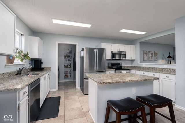 kitchen featuring white cabinets, light stone counters, a kitchen breakfast bar, stainless steel appliances, and a sink