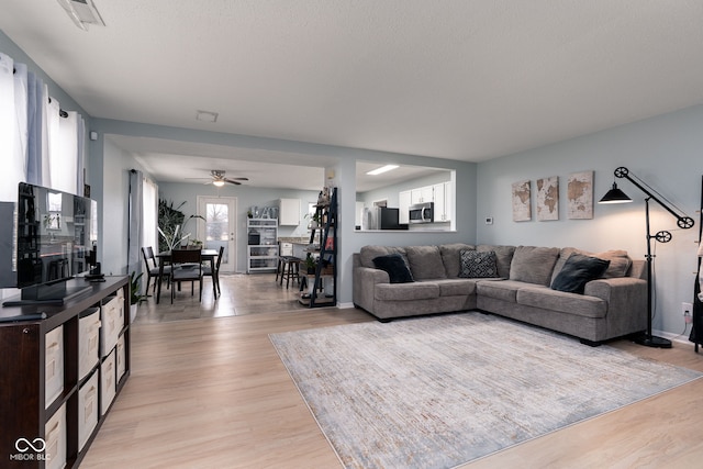 living area featuring light wood finished floors, baseboards, visible vents, and a ceiling fan