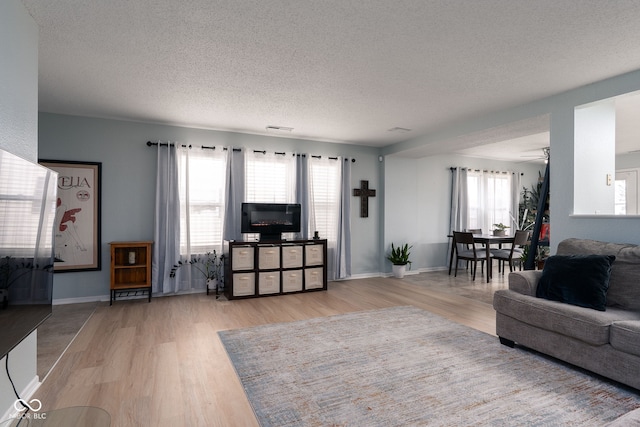 living room with light wood-style flooring, visible vents, baseboards, and a textured ceiling