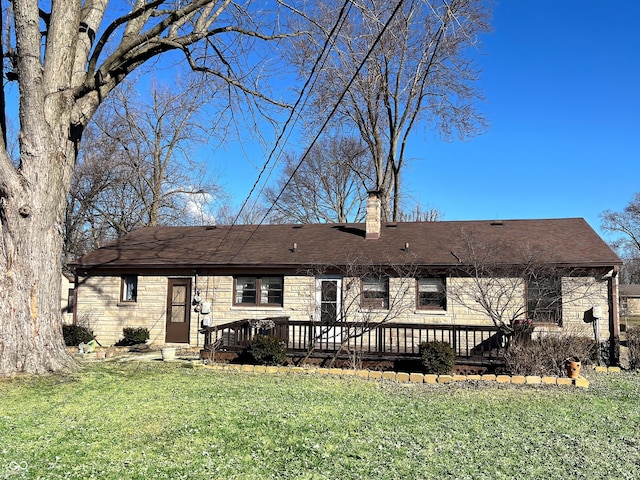 back of property featuring a shingled roof, stone siding, a chimney, a deck, and a yard