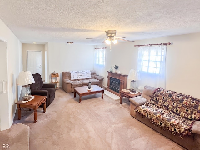 living room featuring a fireplace with raised hearth, ceiling fan, a textured ceiling, and light colored carpet