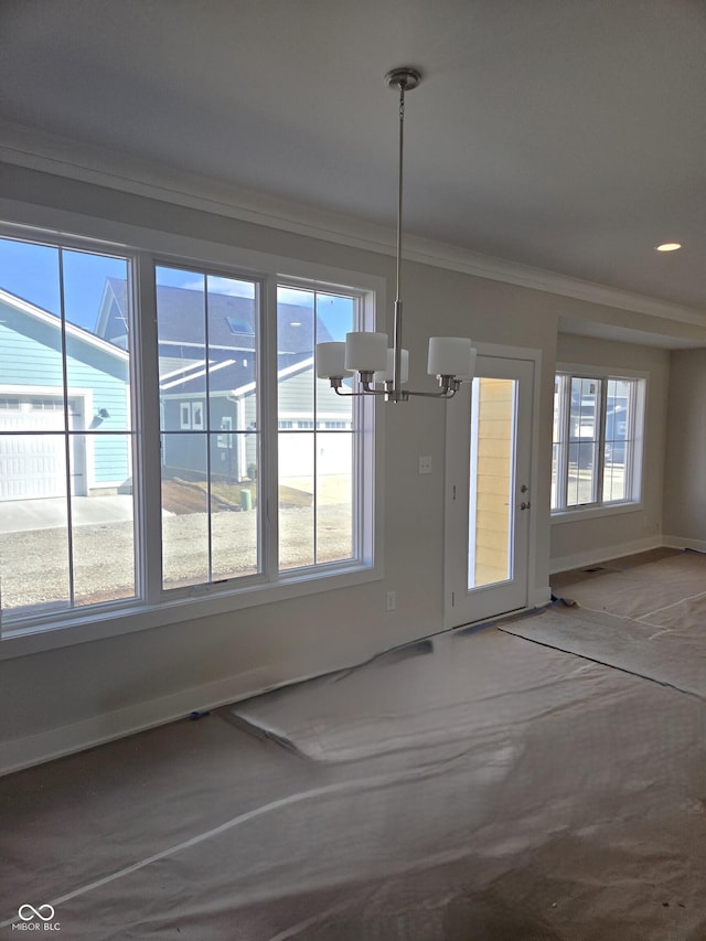 unfurnished dining area featuring a chandelier, ornamental molding, plenty of natural light, and baseboards