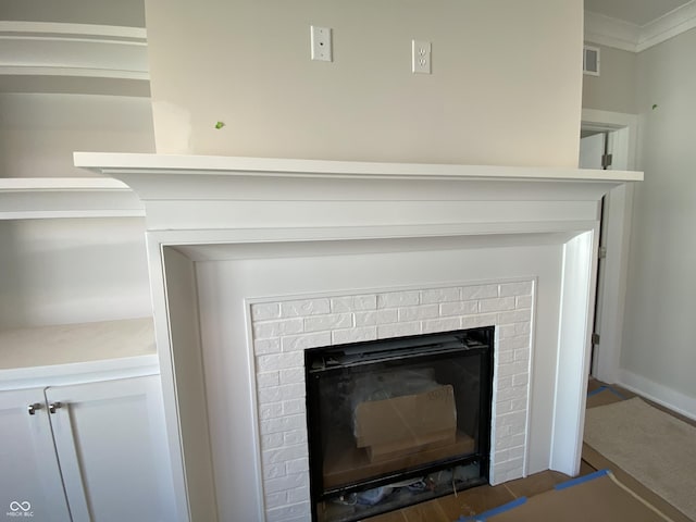 interior details with a brick fireplace, visible vents, wood finished floors, and ornamental molding