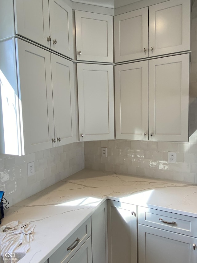 kitchen featuring light stone counters, backsplash, and white cabinetry